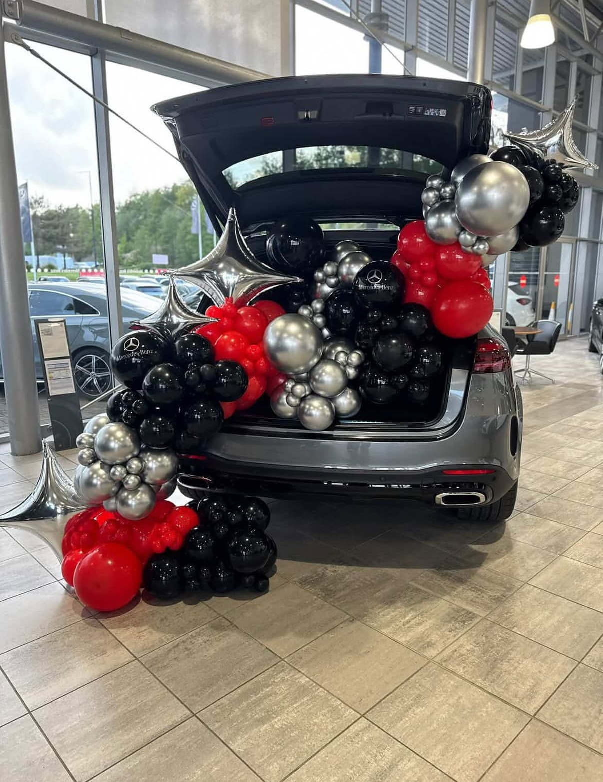 Red, black and silver balloon garland spilling from a Mercedes-Benz dealership car trunk display