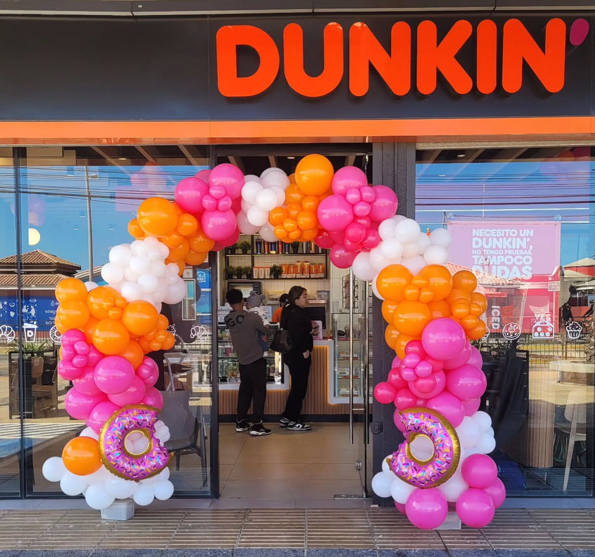 Pink, orange and white balloon arch at a Dunkin' storefront grand opening